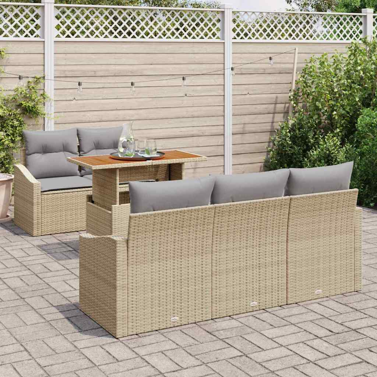 Gartenmöbel-Set aus Korbgeflecht mit grauen Kissen und Holztisch. Ein weißer Gitterzaun und Grün im Hintergrund.