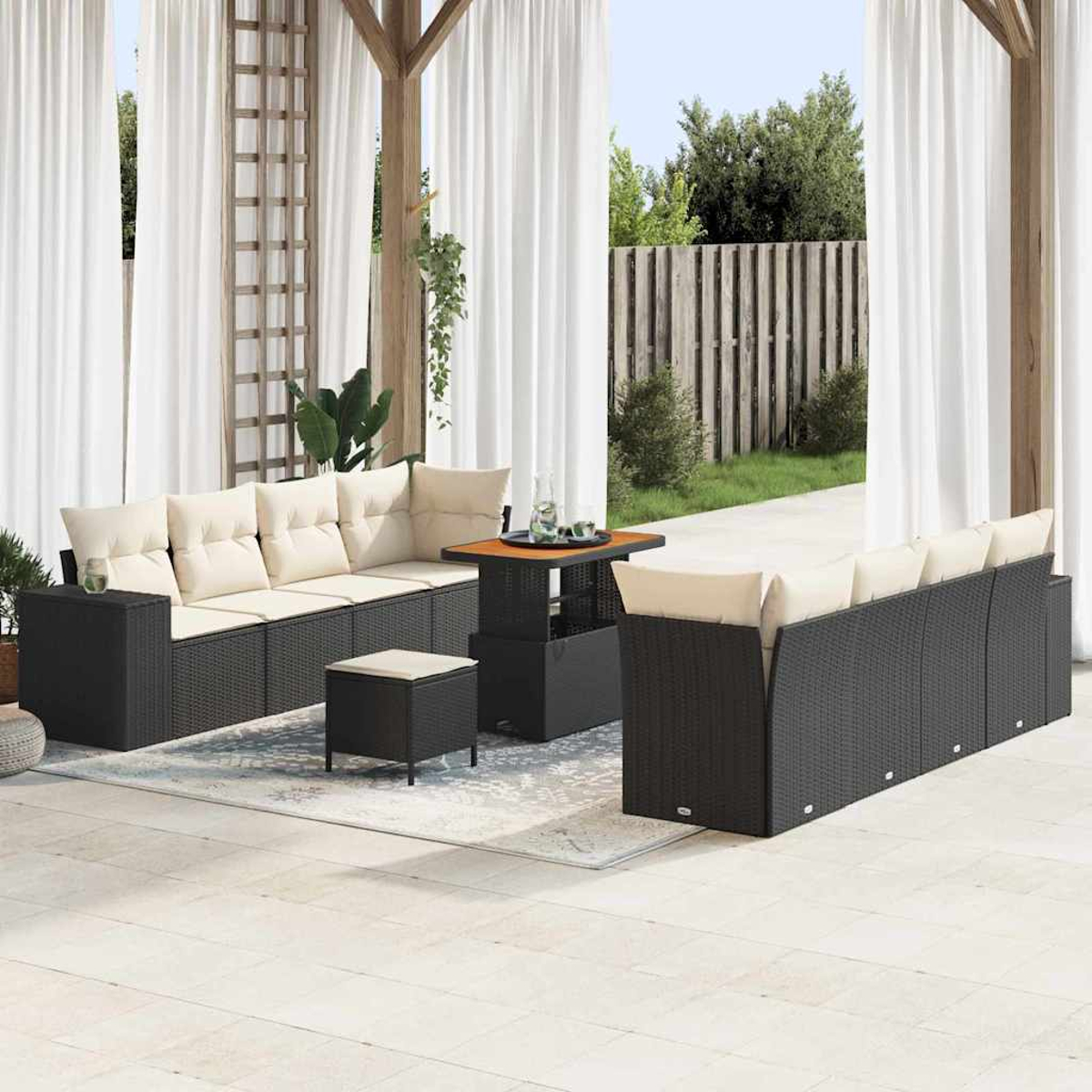 Terrassenmöbel mit schwarzen Korbsessel, beigen Kissen, kleinem Tisch und Hocker auf einem Teppich, umrahmt von weißen Vorhängen.