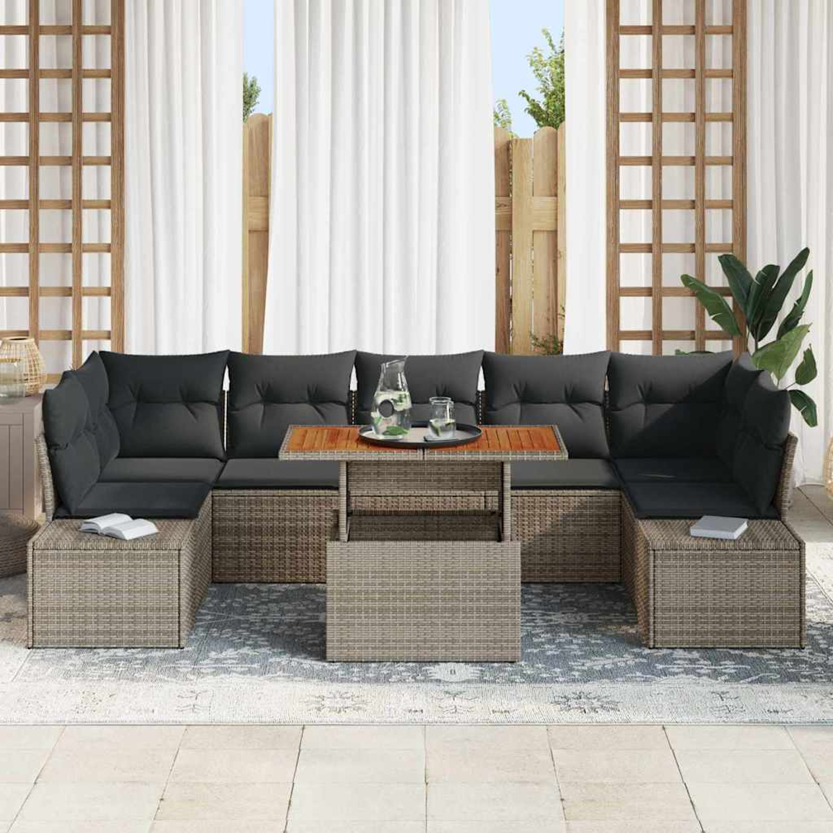 Ein Ecksofa im Freien mit dunklen Kissen. Ein Holztisch mit einem Glas Wasser und einem Krug. Weiße Vorhänge im Hintergrund.