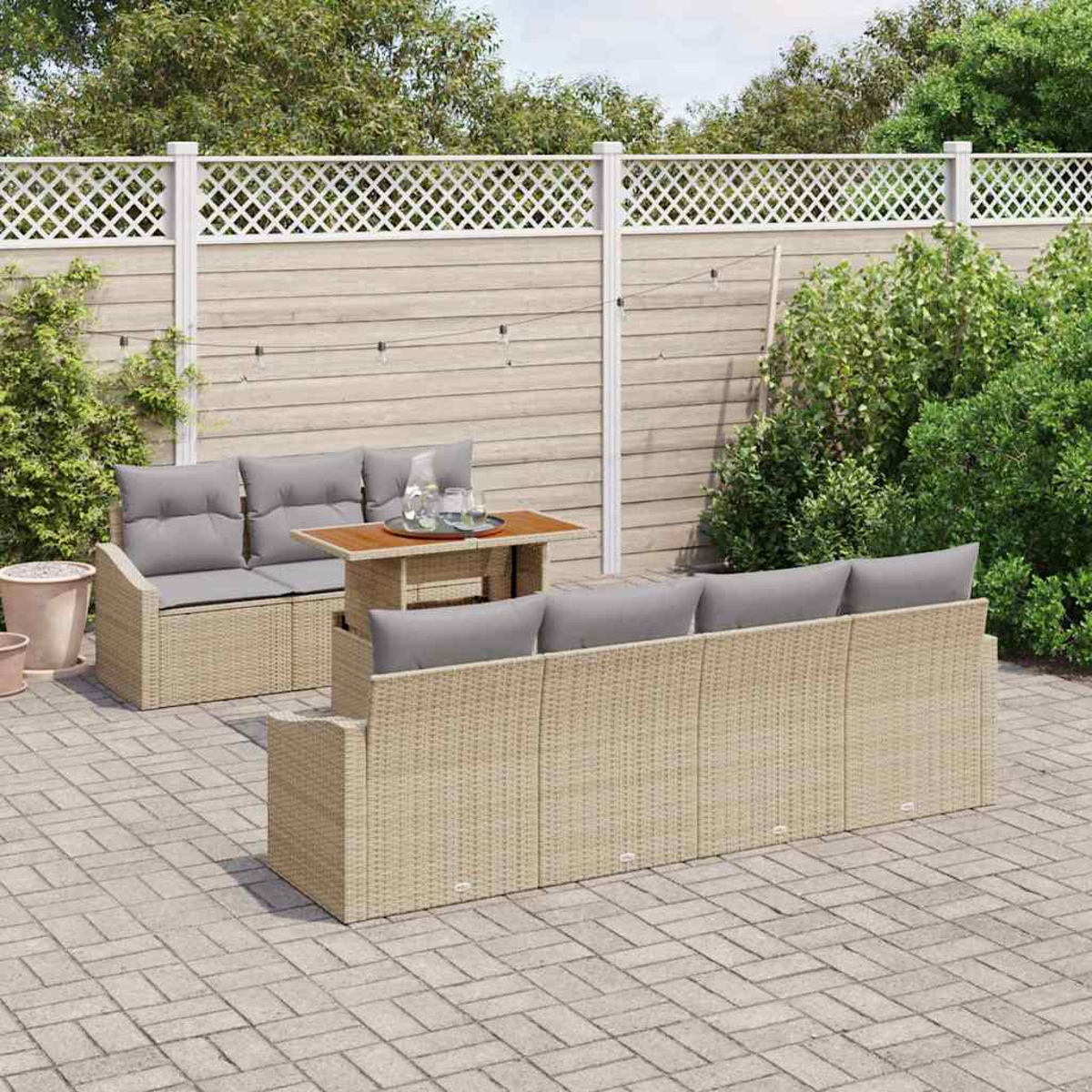 Szene im Freien mit Korbmöbeln, grauen Kissen, einem kleinen Tisch und einem Holzzaun auf einer gefliesten Terrasse mit Grün.
