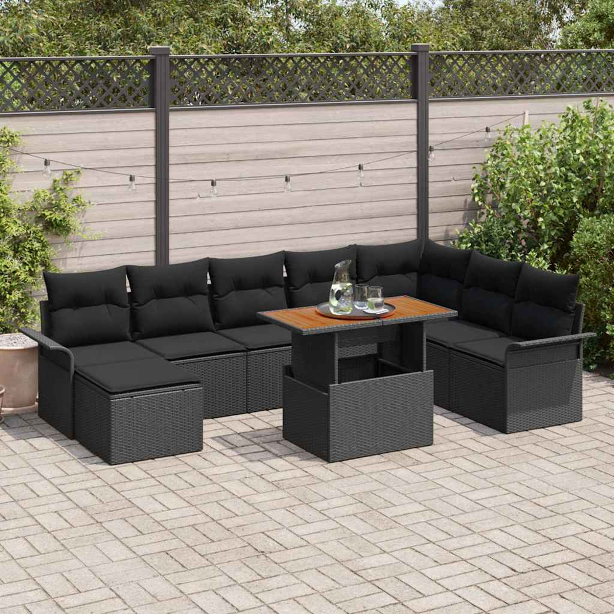 Garten-Terrassenset mit schwarzen Kissen, einem Holztisch und einer Ziegelterrasse. Im Hintergrund ein Zaun und Grün.