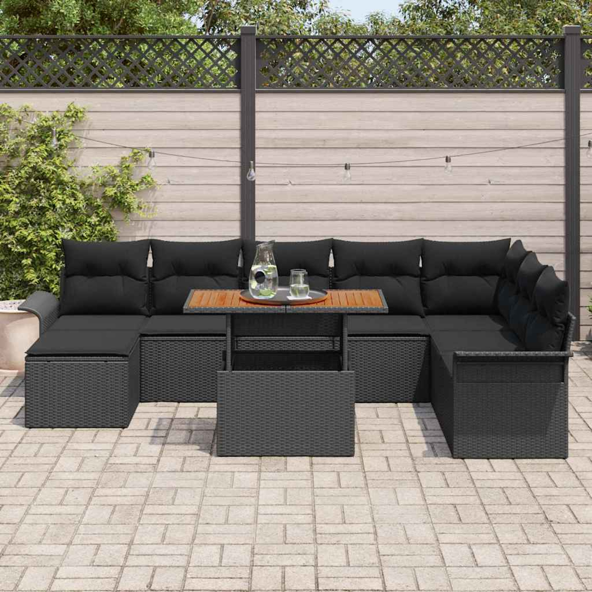 Outdoor-Ecksofa mit schwarzen Kissen und einem Holztisch. Ein Glas Wasser und eine Kanne stehen auf dem Tisch. Der Hintergrund ist ein Zaun.
