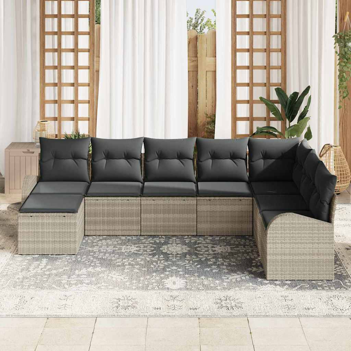 Ecksofa im Freien mit grauen Kissen auf einem gemusterten Teppich, vor weißen Vorhängen und Holzgitter.