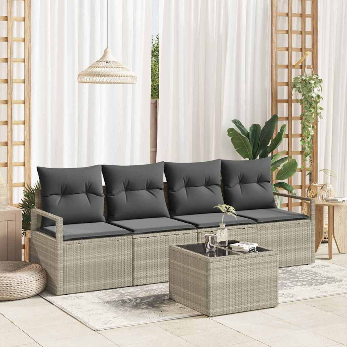 Ein graues Rattansofa mit dunkelgrauen Kissen und einem passenden Couchtisch vor einem weißen Vorhang.