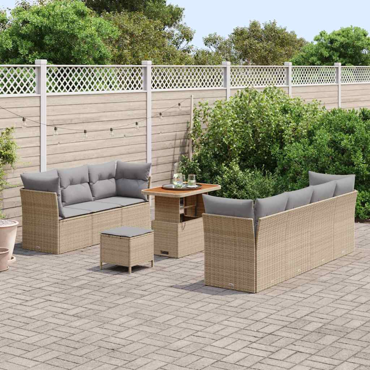 Gartenmöbel-Set. Enthält Sofas mit grauen Kissen, einen kleinen Tisch und einen Hocker auf einer gepflasterten Terrasse, mit Zaun im Hintergrund.