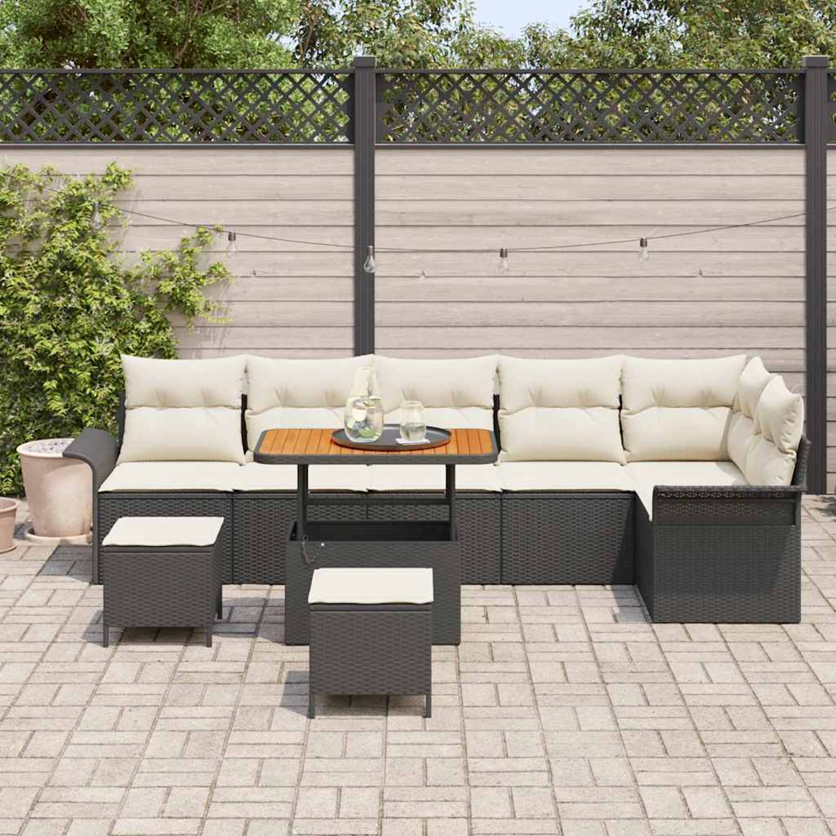 Ein Outdoor-Terrassenset mit grauen Korbmöbeln, beigen Kissen und einem kleinen Tisch. Ein Holzzaun und Grün bilden den Hintergrund.
