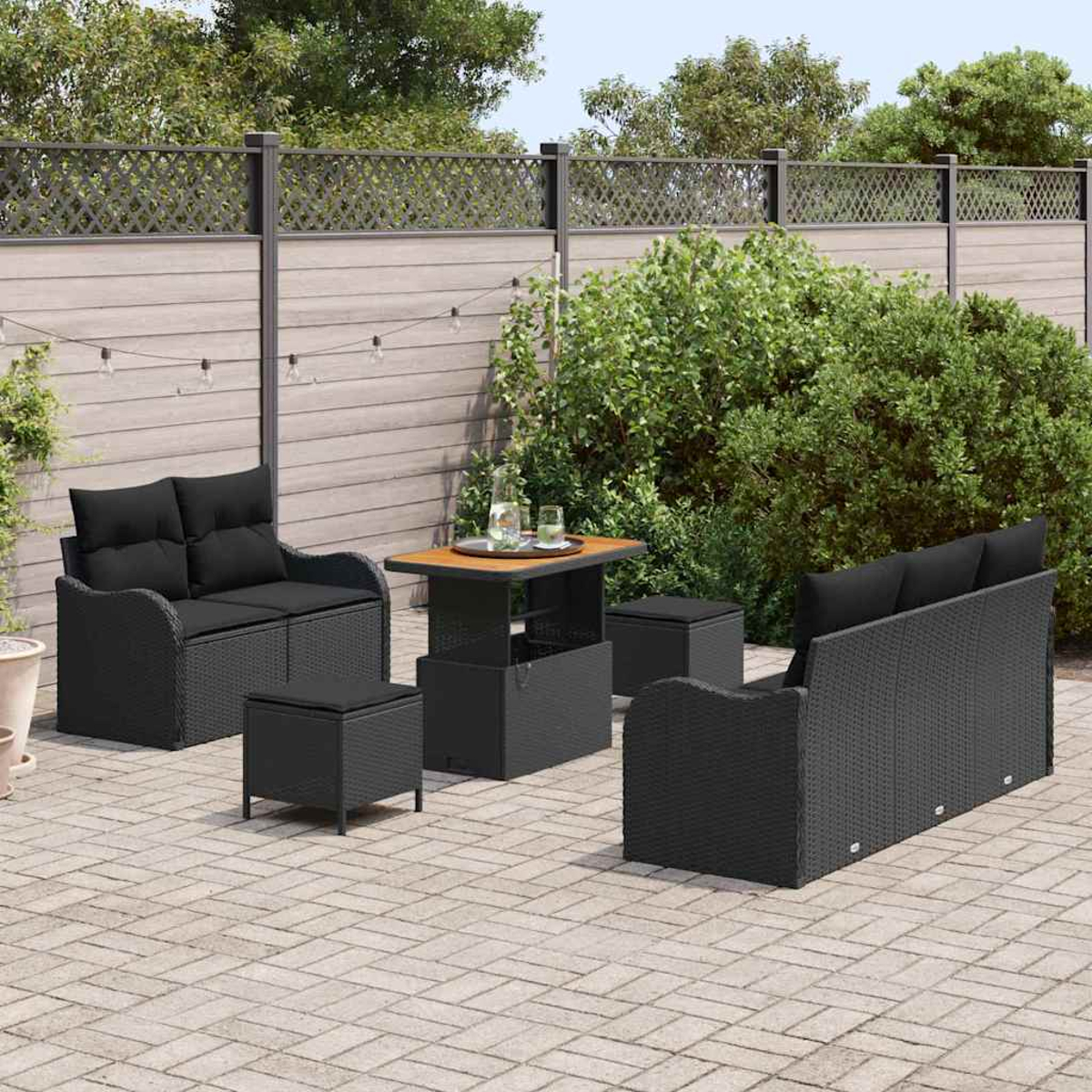 Garten-Terrassenset mit schwarzen Korbmöbeln auf einer Ziegelterrasse, darunter ein Sofa, eine Loveseat, ein Tisch und zwei Hocker. Grünes Laub im Hintergrund.