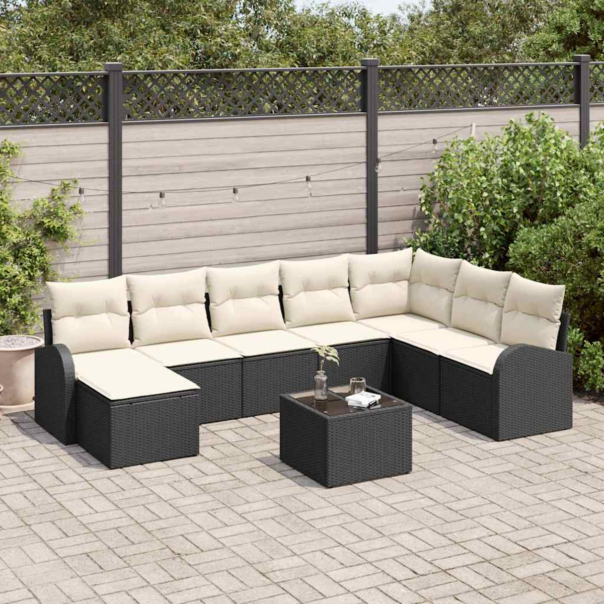 Outdoor-Ecksofa mit cremefarbenen Kissen und schwarzen Rahmen. Davor ein kleiner Tisch. Im Hintergrund ein Zaun und Grün.