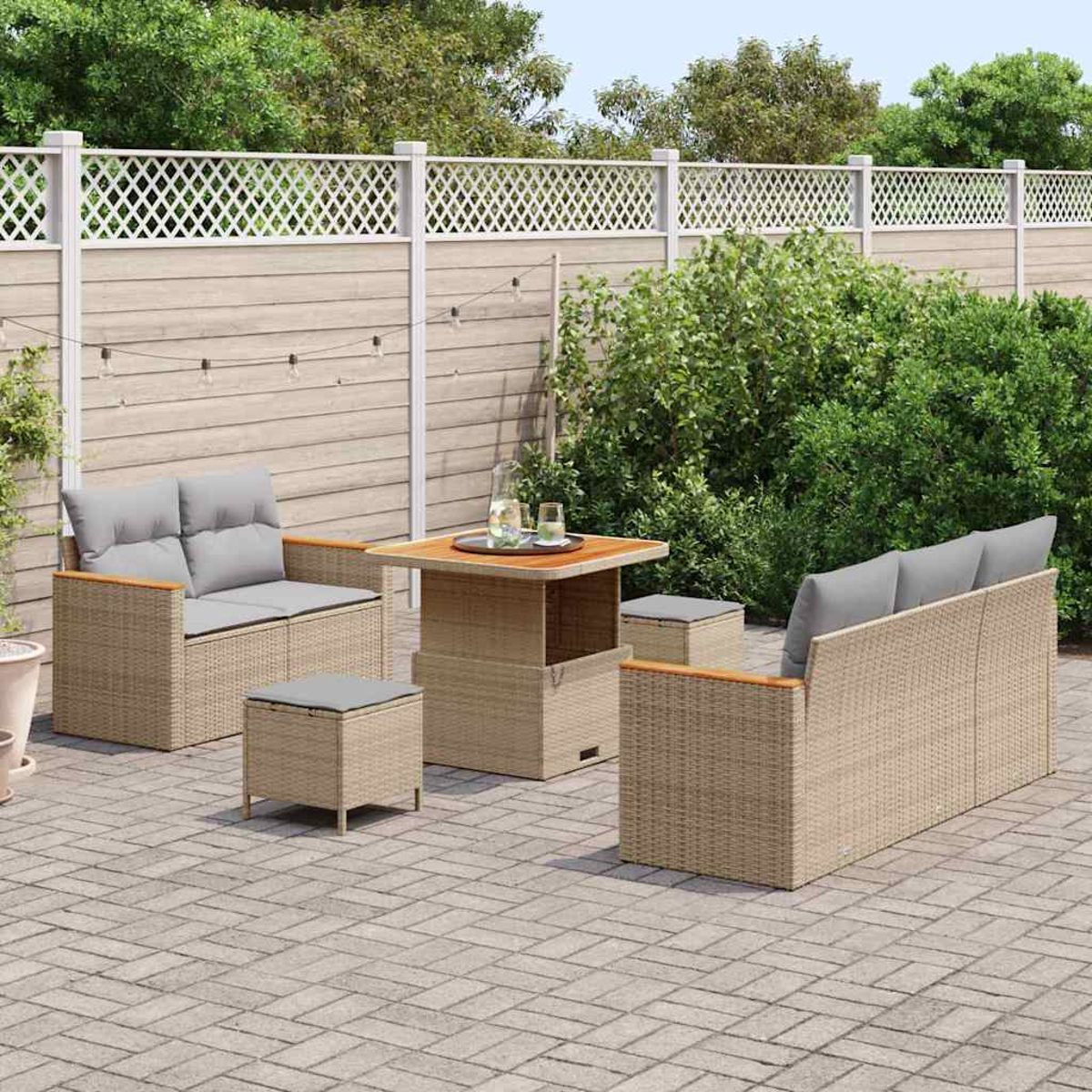 Terrassenset mit Korbmöbeln, grauen Kissen, einem quadratischen Tisch und einem Zaun im Hintergrund.