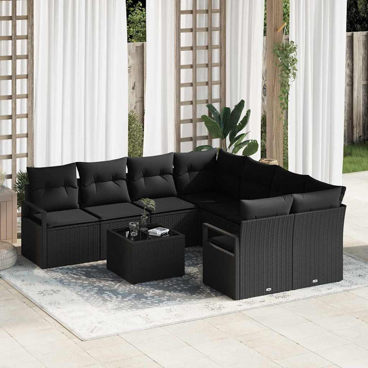Outdoor-Set aus schwarzem Korbgeflecht mit Kissen, Couchtisch, auf einem Teppich, mit weißen Vorhängen im Hintergrund.