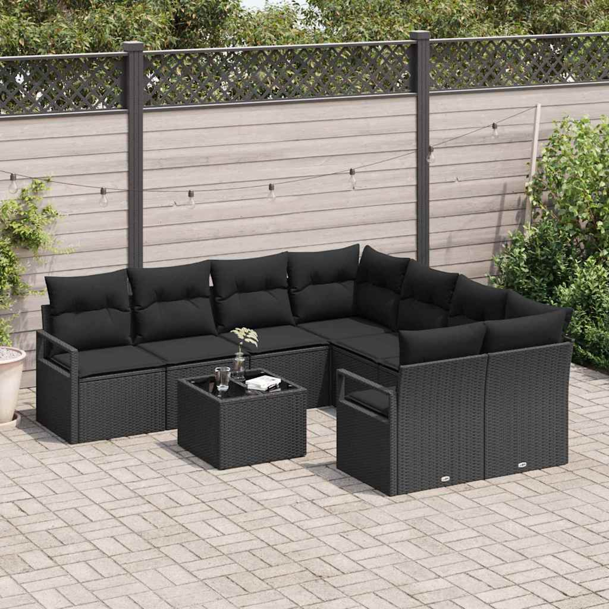 Garten-Terrasseneinrichtung mit schwarzen Korbmöbeln. Ein Ecksofa, ein kleiner Tisch und ein Sessel stehen auf einer Backsteinterrasse.