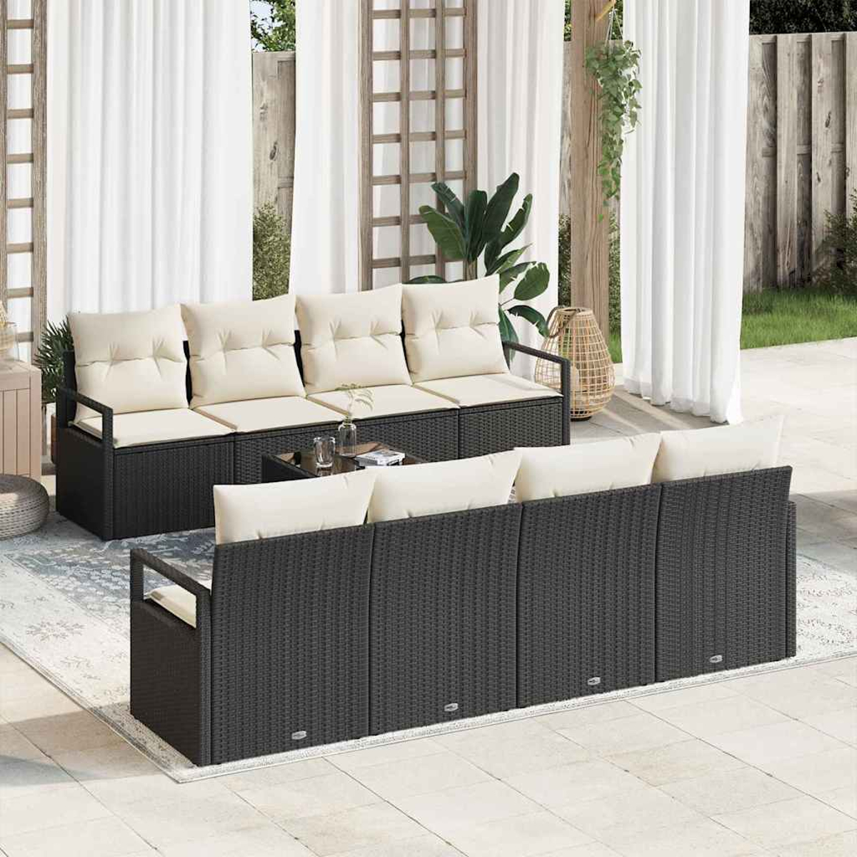 Garten-Set mit schwarzen Korbs Sofas, cremefarbenen Kissen und einem Glastisch. Weiße Vorhänge und ein Garten im Hintergrund.