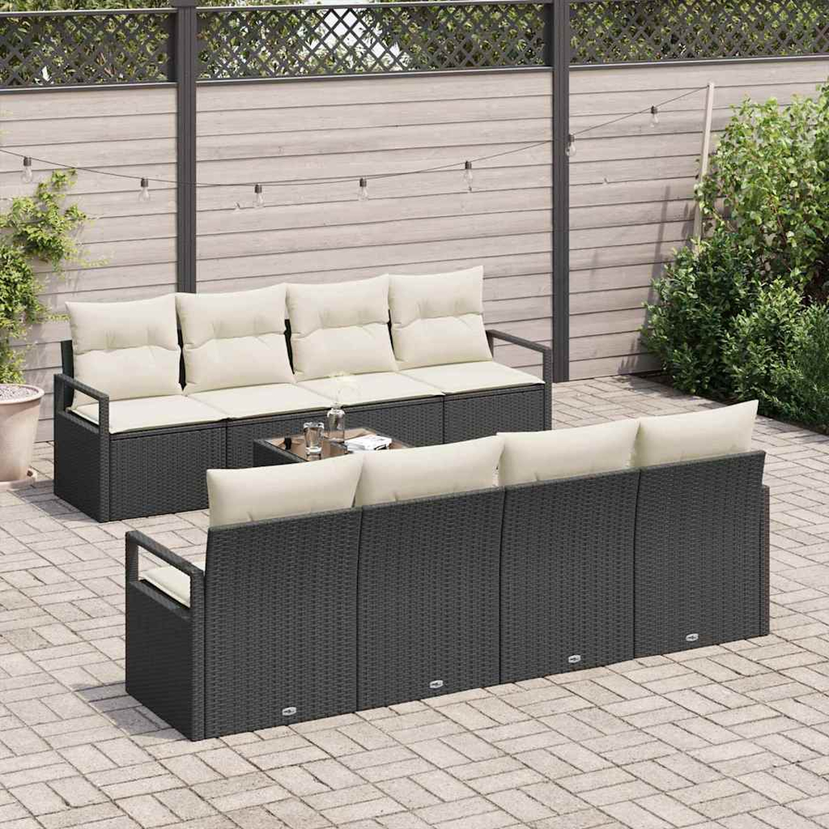 Outdoor-Terrassenset mit dunkelgrauen Korbsesseln, cremefarbenen Kissen und einem Tisch mit Glasplatte. Auf einer Ziegelterrasse mit Holzzaun im Hintergrund.
