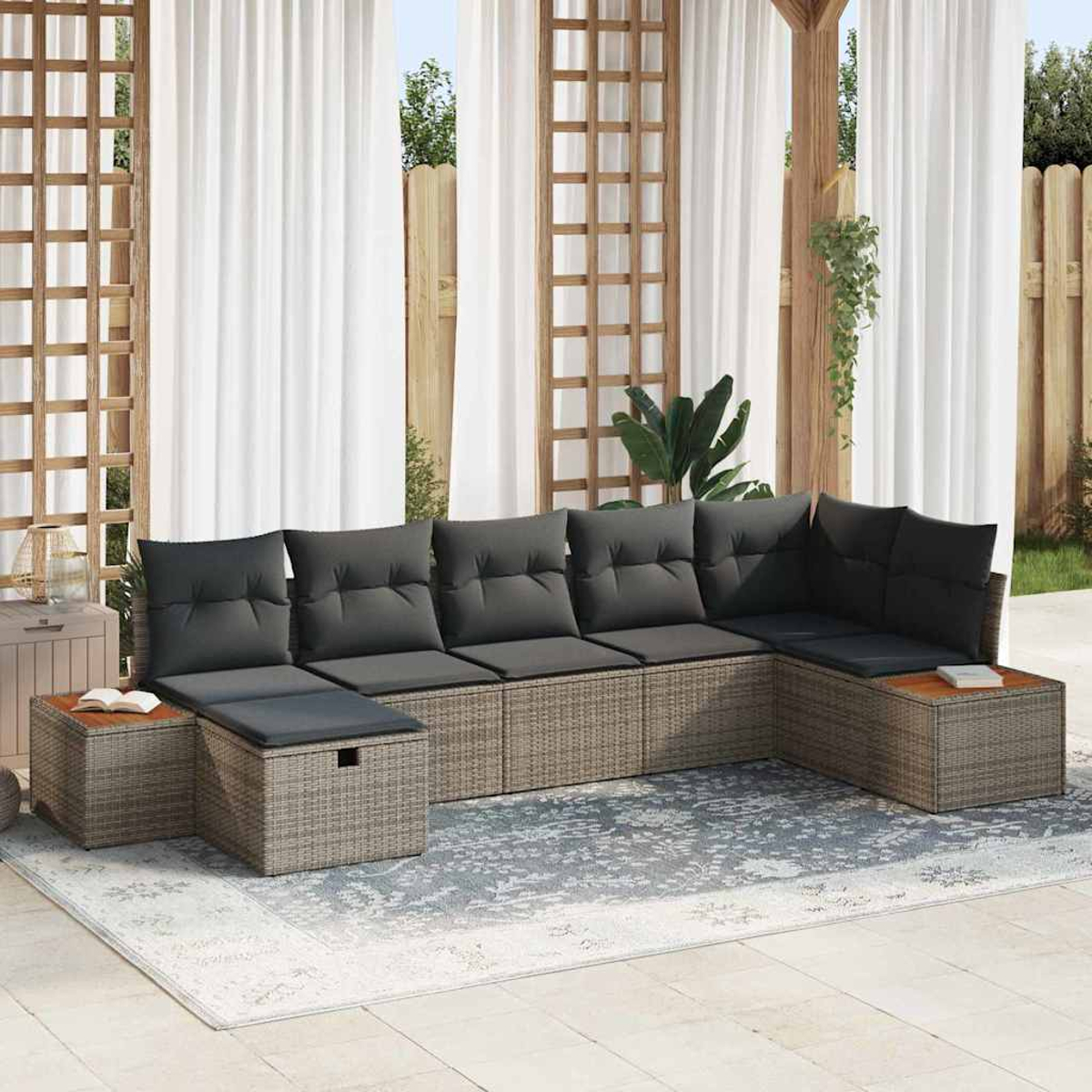 Outdoor-Ecksofa mit grauen Kissen auf einem gemusterten Teppich. Weiße Vorhänge im Hintergrund. Holzbeistelltische und Spalier sind sichtbar.