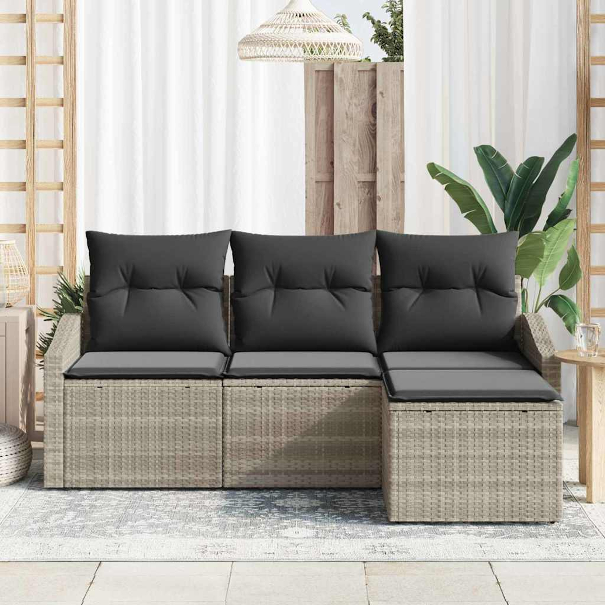 Ein Outdoor-Sofa aus Korbgeflecht mit grauen Kissen steht auf einem Teppich. Eine gewebte Lampe hängt darüber. Der Hintergrund umfasst einen Zaun und Pflanzen.