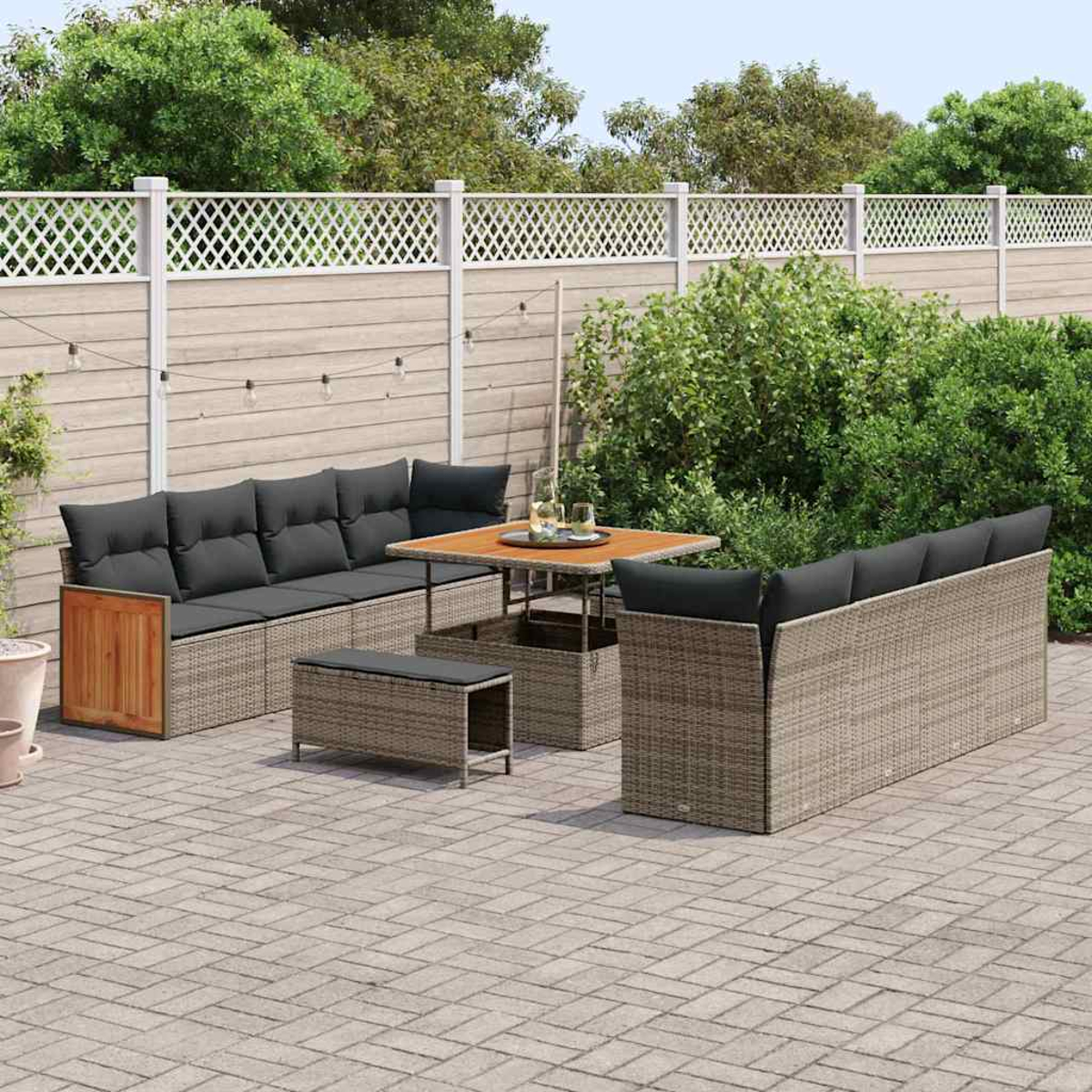 Gartenmöbel-Set auf einer Ziegelterrasse. Beinhaltet ein Sofa, Tisch, Bank und ein weiteres Sofa. Weißer Zaun und Grün im Hintergrund.