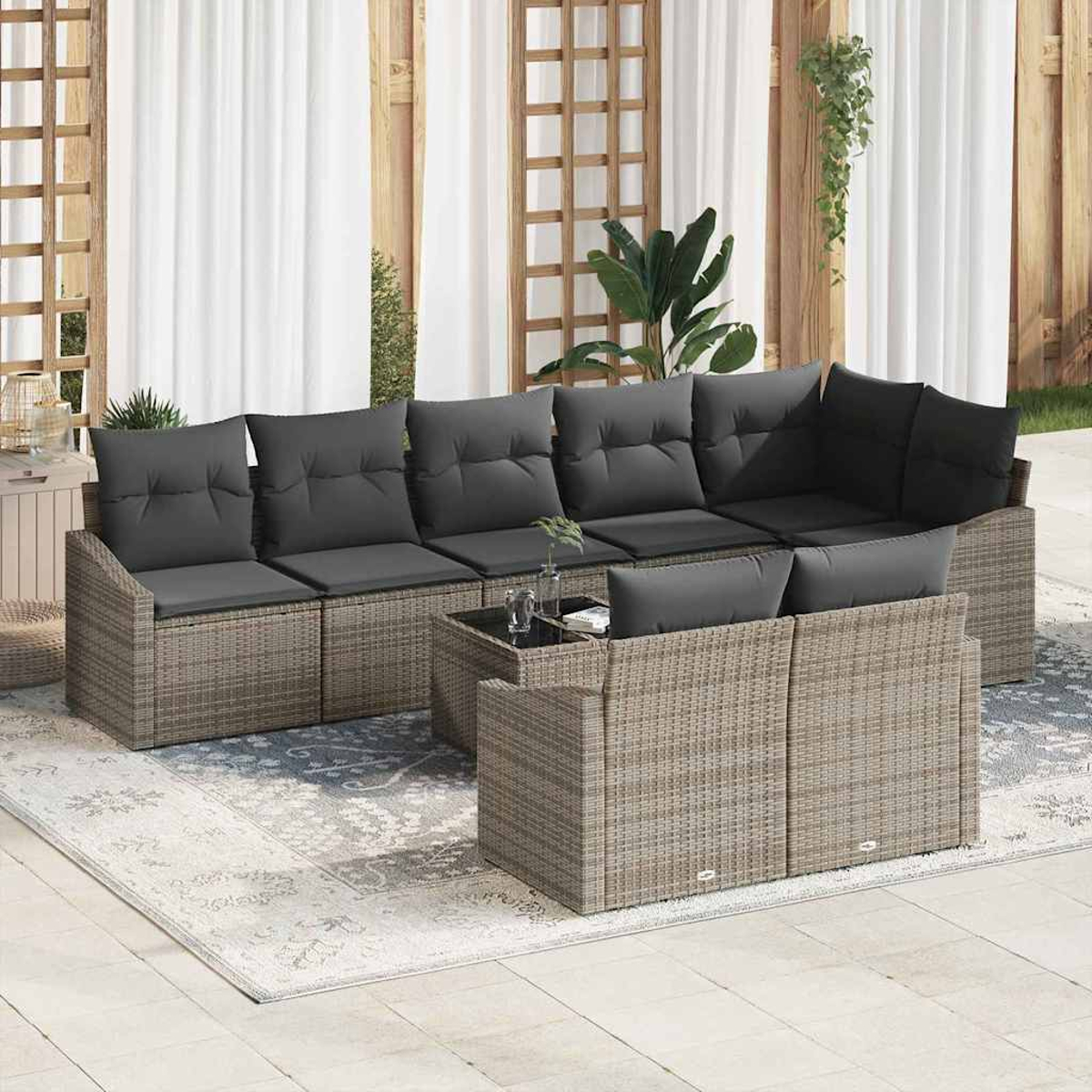 Outdoor-Ecksofa mit grauen Kissen auf einem gemusterten Teppich. Ein Glastisch mit Pflanzen steht davor. Vorhänge und Holzpaneele im Hintergrund.
