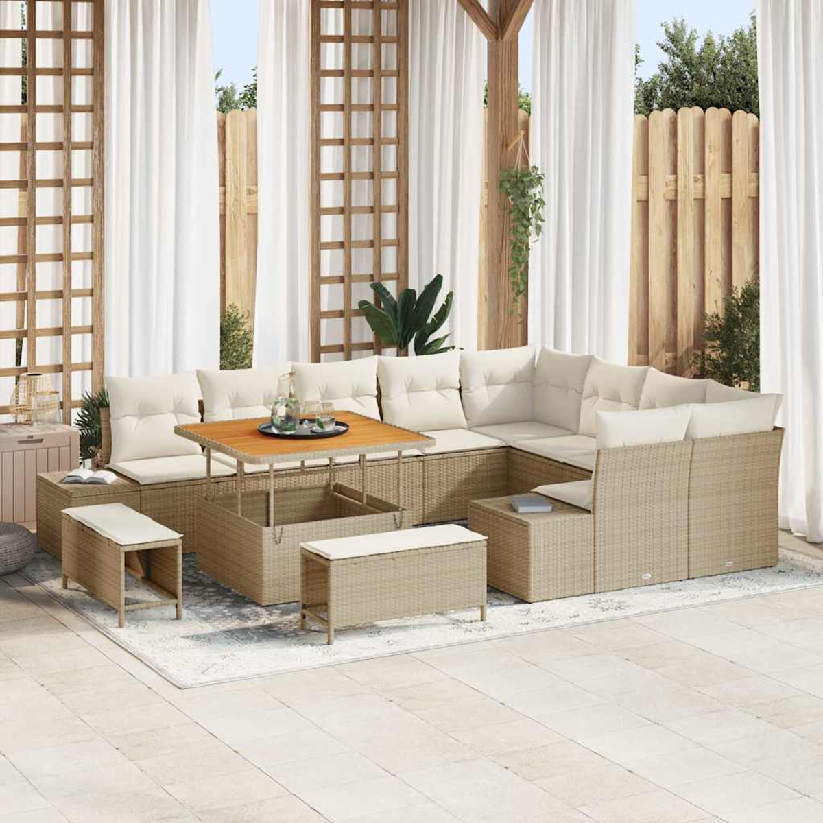 Outdoor-Wicker-Sofa mit beigen Kissen, Holztisch und passenden Bänken. Auf einem Teppich, mit weißen Vorhängen und einem Holzzaun im Hintergrund.