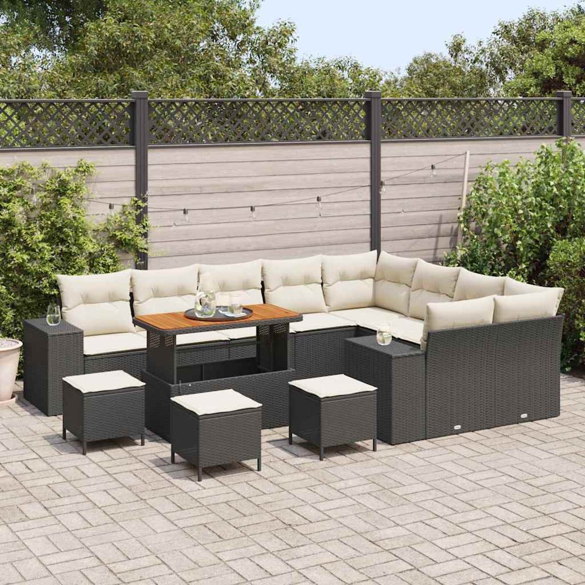Divano componibile da esterno con cuscini beige, un tavolo in legno con bicchieri e sgabelli quadrati su un patio in pietra, con una recinzione sullo sfondo.