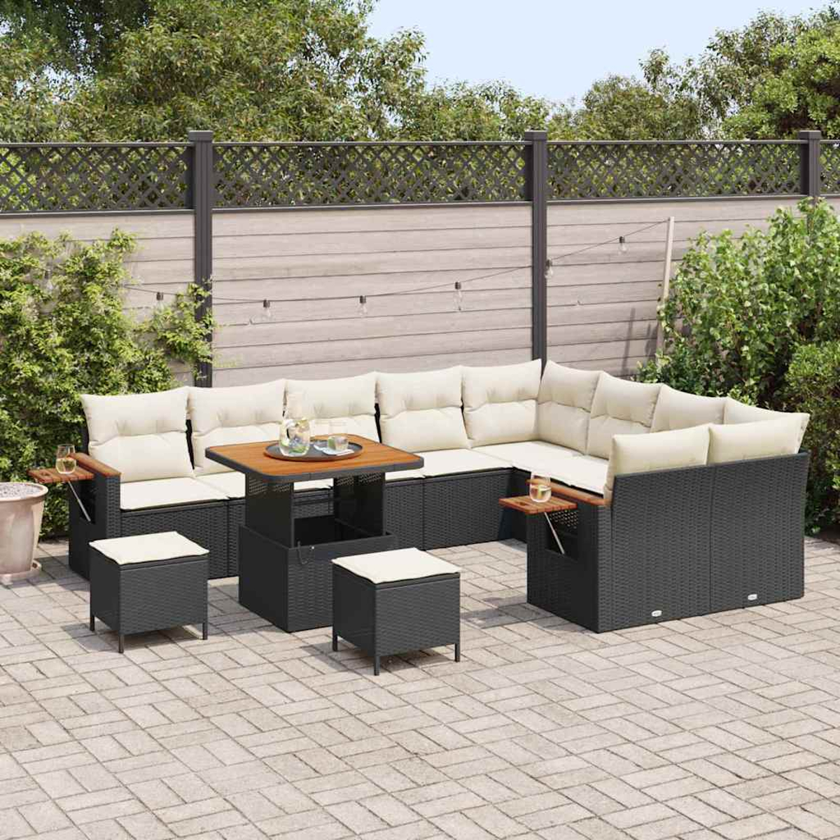 Outdoor-Ecksofa mit Kissen, Tisch und Hockern auf einer Terrasse. Im Hintergrund ein Zaun und Grün.