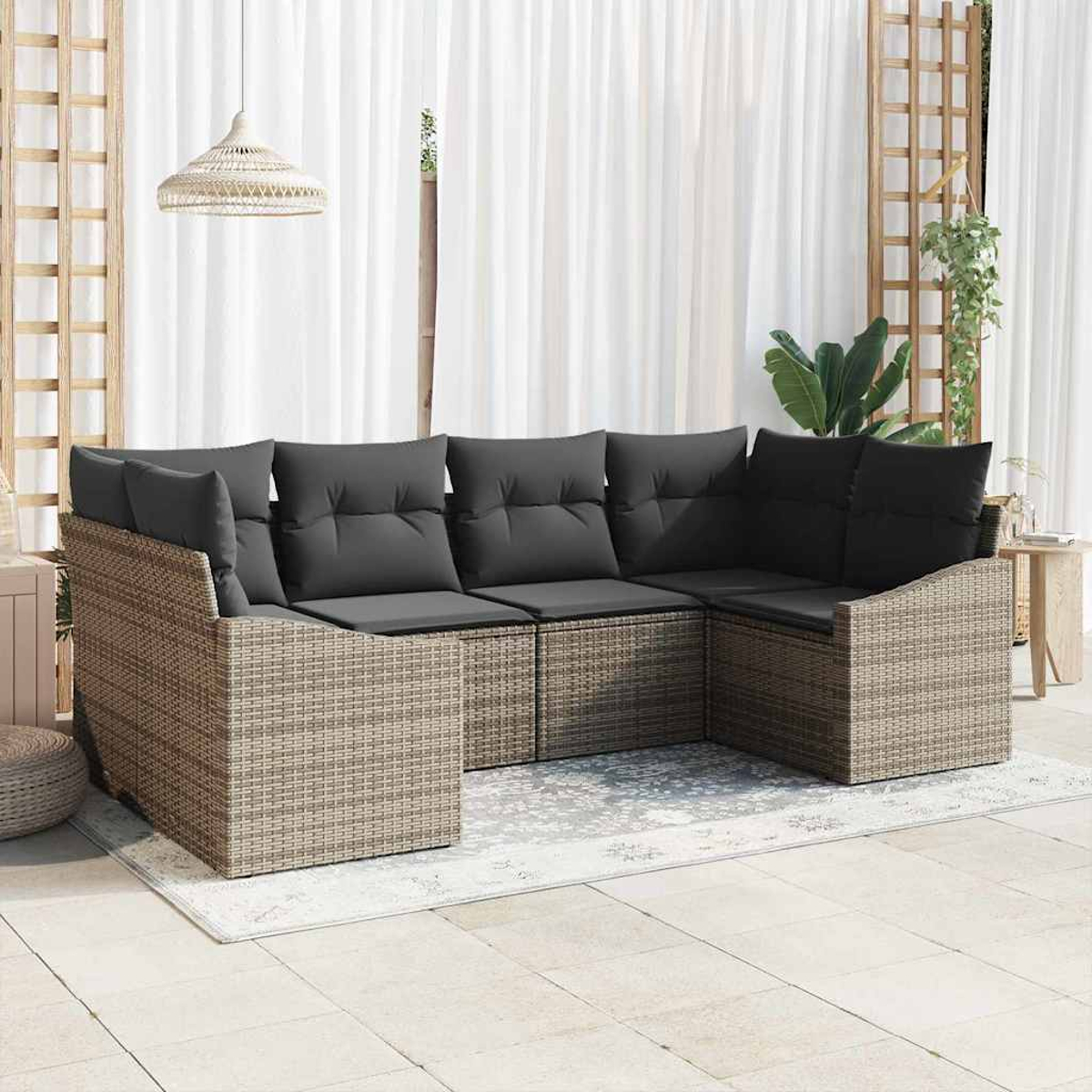 Ein Ecksofa aus Korbgeflecht mit grauen Kissen steht auf einem Teppich. Weiße Vorhänge und eine Hängeleuchte sind im Hintergrund.