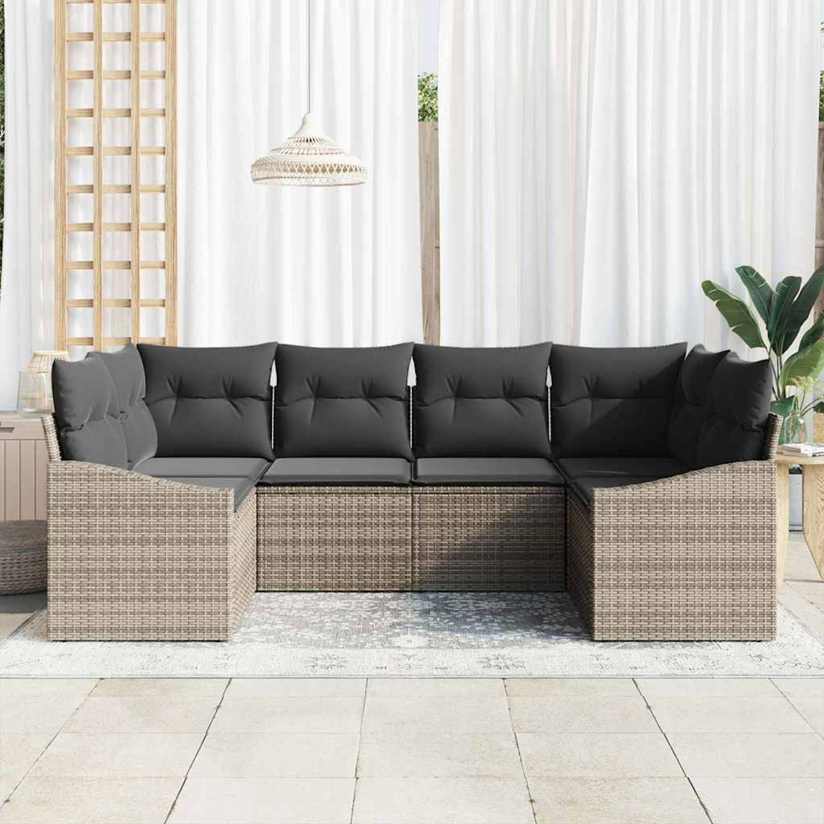 Outdoor-Rattansofa mit grauen Kissen. Dahinter weiße Vorhänge und eine Hängeleuchte. Rechts eine Pflanze.
