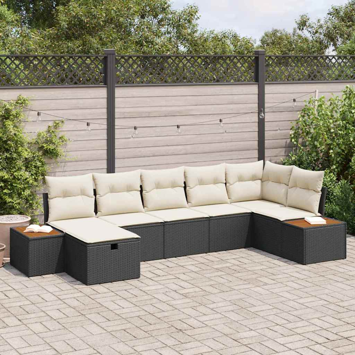 Ein schwarzes Rattan-Außensofa mit cremefarbenen Kissen steht auf einer gepflasterten Terrasse. Ein Holztisch und ein Zaun befinden sich im Hintergrund.