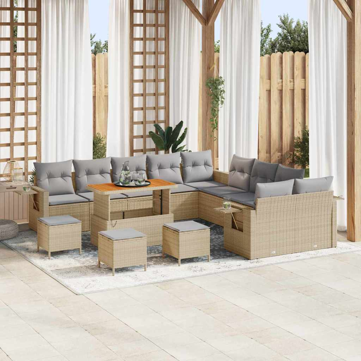 Outdoor-Sitzbereich mit Korbmöbeln, grauen Kissen, Holztisch und Vorhängen. Enthält Hocker und einen Teppich. Im Hintergrund sind Zaun und Bäume zu sehen.