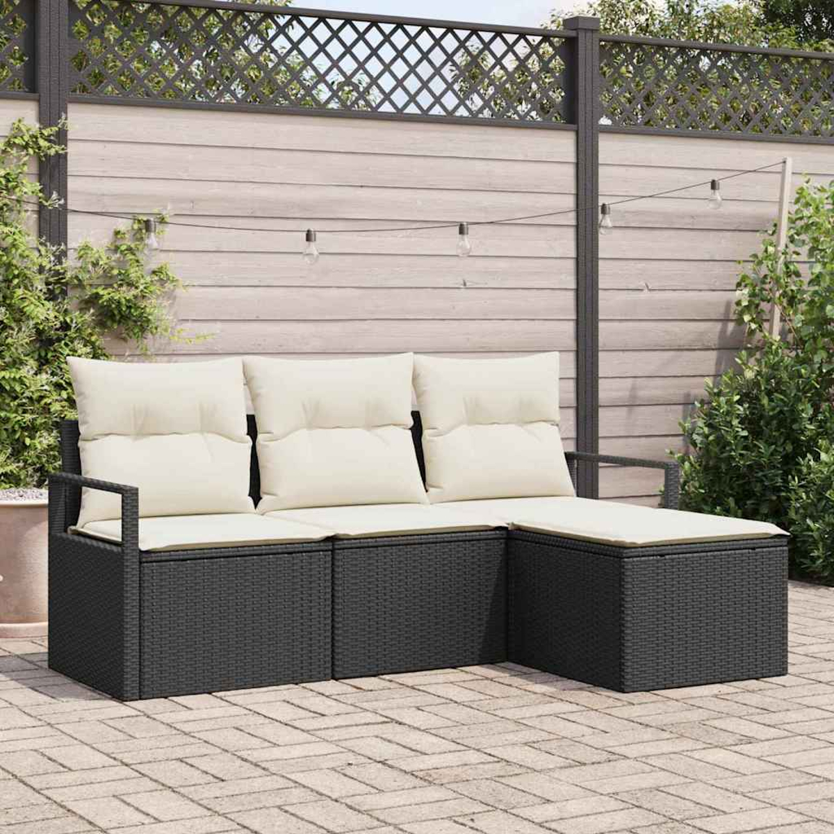 Ein schwarzes Outdoor-Rattansofa mit cremefarbenen Kissen. Im Hintergrund ein Holzzaun und dekorative Lichter.