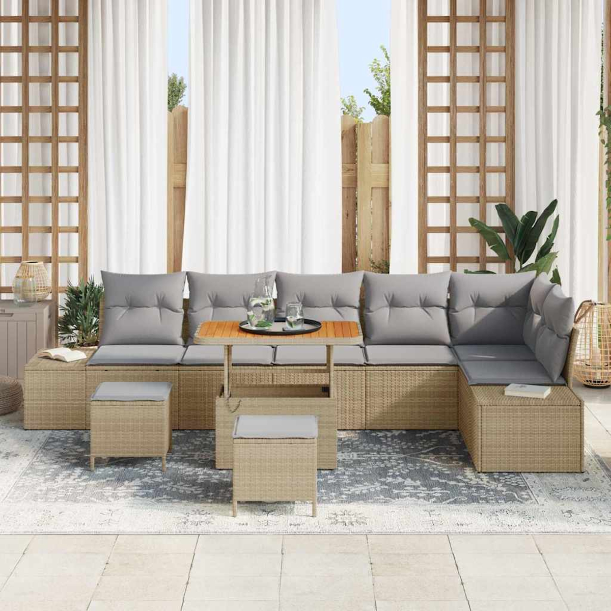 Outdoor-Sitzgruppe mit grauen Kissen, kleinem Tisch und zwei Hockern auf einem gemusterten Teppich, weiße Vorhänge im Hintergrund.