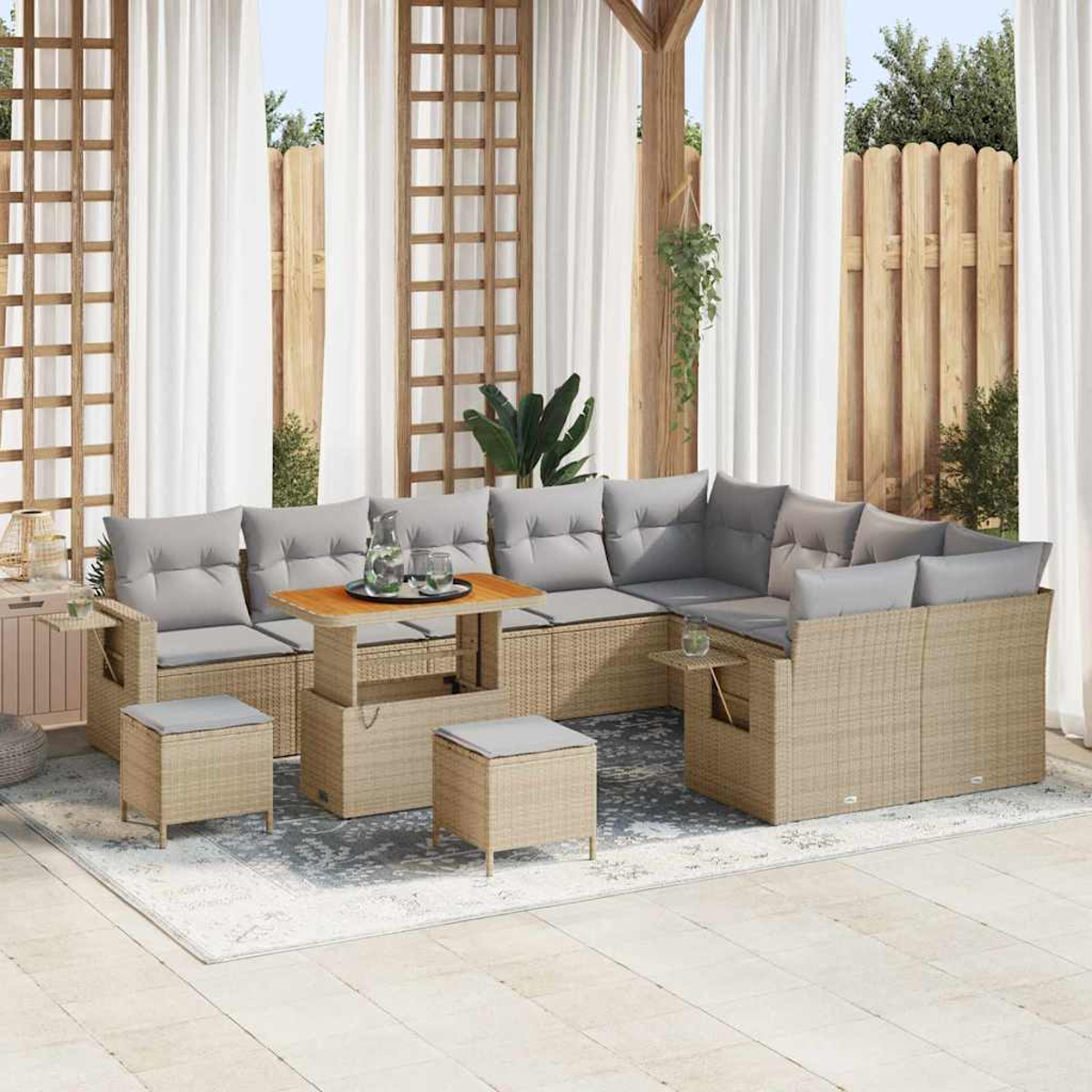 Outdoor-Ecksofa mit grauen Kissen, Holztisch und Hockern auf einem gemusterten Teppich. Weiße Vorhänge und Holzzaun im Hintergrund.