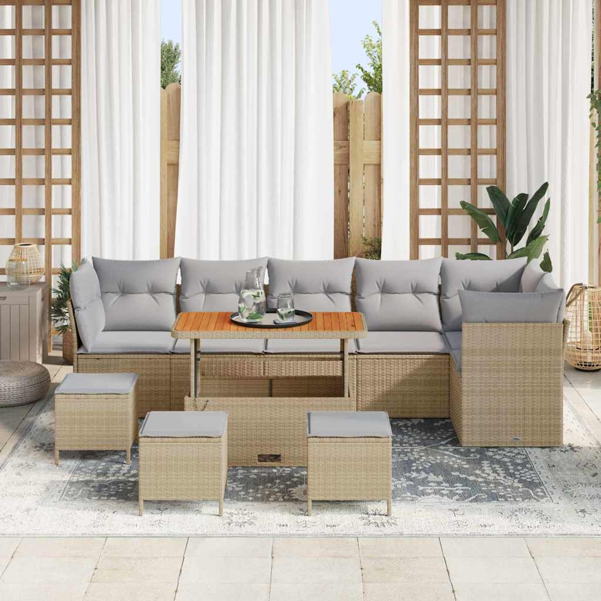 Terrassenset mit beigen Korbmöbeln, grauen Kissen und einem Holztisch, auf einem gemusterten Teppich, mit weißen Vorhängen im Hintergrund.