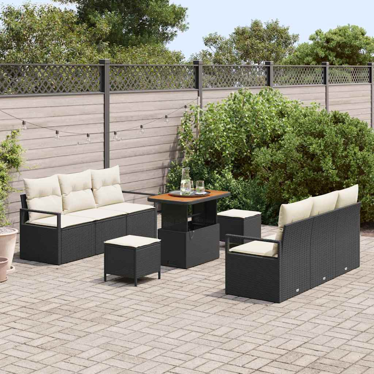 Juego de patio al aire libre con muebles de mimbre negros, cojines beige y una mesa. El fondo presenta una valla, vegetación y un patio de ladrillos.