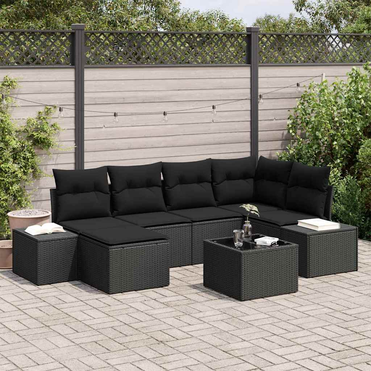 Ein schwarzes Outdoor-Ecksofa aus Korbgeflecht mit schwarzen Kissen, einem Couchtisch und zwei Ottomanen steht auf einer Backsteinterrasse.