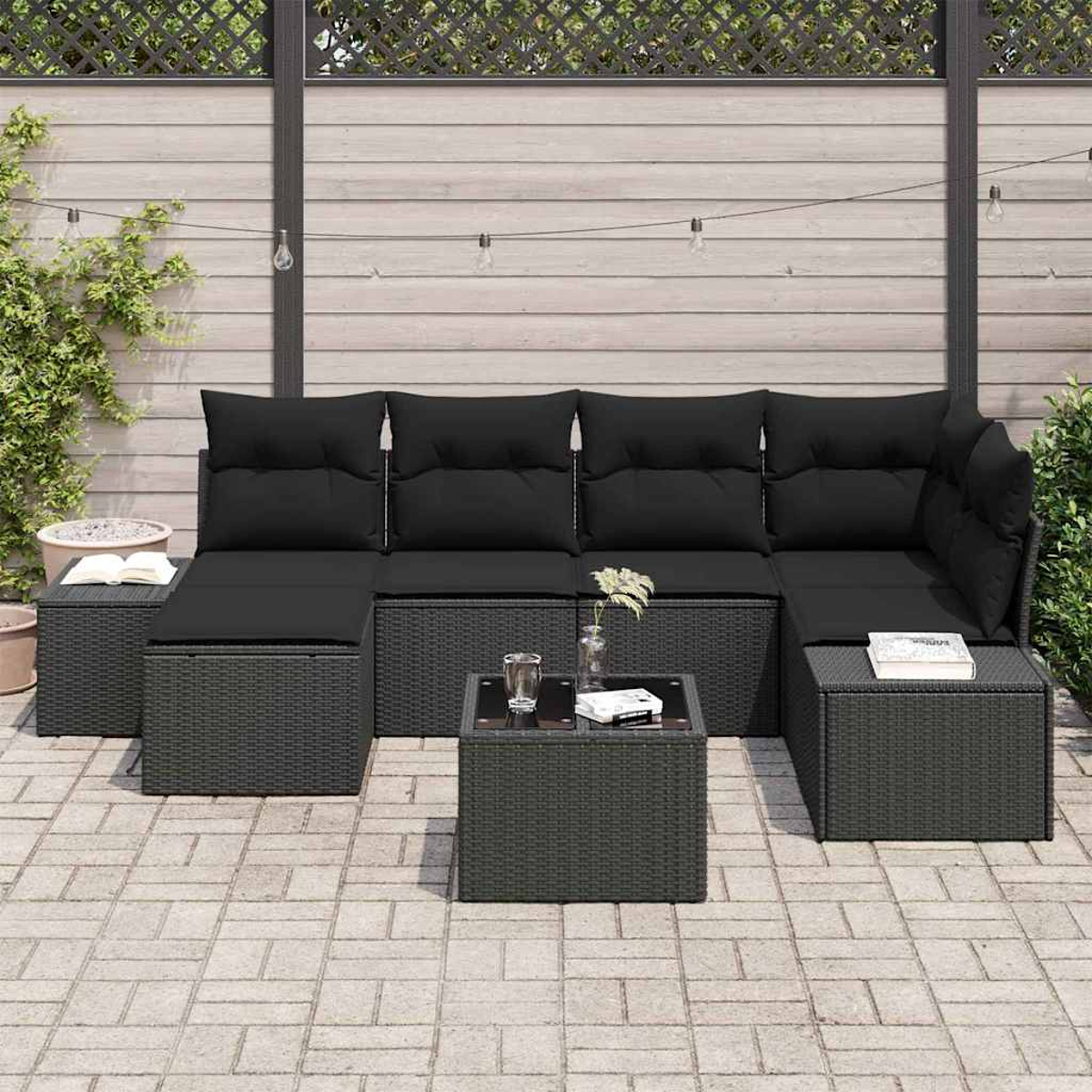Garten-Sitzgruppe mit schwarzen Kissen und einem kleinen Tisch. Das Set befindet sich auf einer Terrasse mit Holzzaun im Hintergrund.