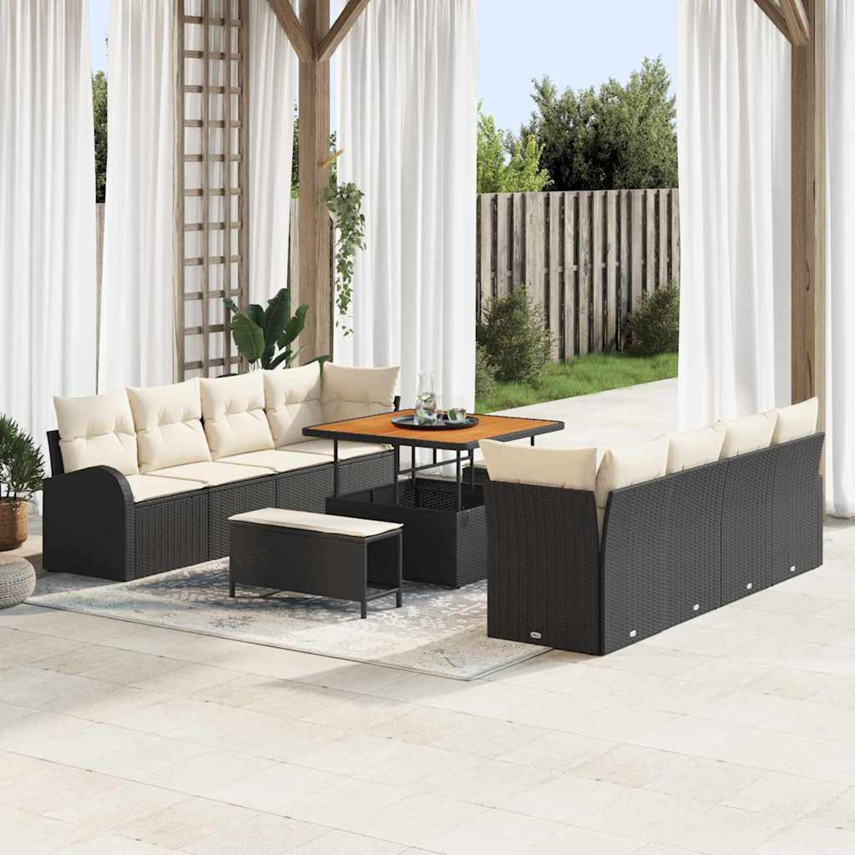 Terrassenset mit schwarzen Korbmöbeln, beigen Kissen und einem Holztisch. Weiße Vorhänge und ein Holzzaun sind im Hintergrund.