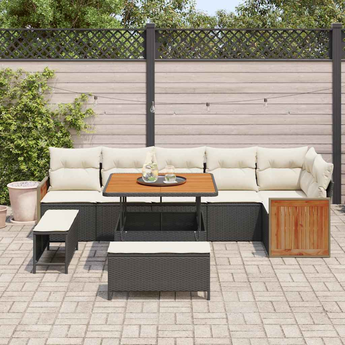 Terrassenset mit Sofa, Tisch und Bänken. Beige Kissen, dunkelgraues Korbgeflecht und Holzakzente. Ziegelpflaster und Holzzaun.