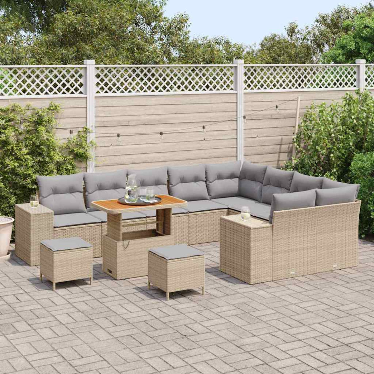 Divano angolare da esterno con cuscini grigi, un tavolo di legno e pouf su un patio. Una recinzione bianca e vegetazione sullo sfondo.