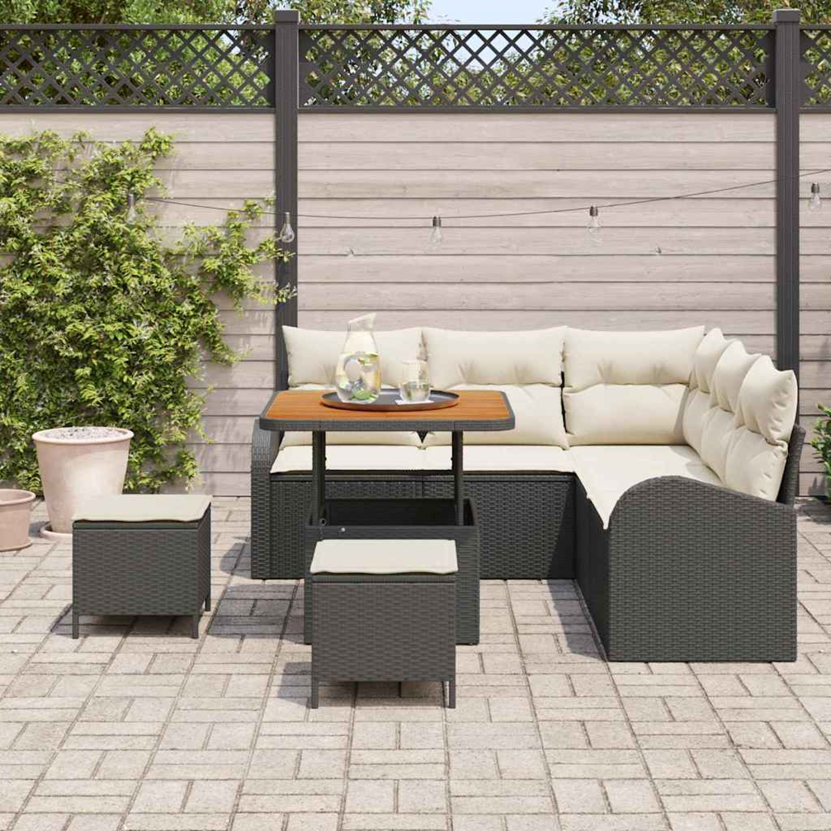 Outdoor-Sitzgruppe mit Tisch, zwei Hockern und Ecksofa. Auf dem Tisch stehen eine Kanne und Gläser. Im Hintergrund ein Holzzaun.