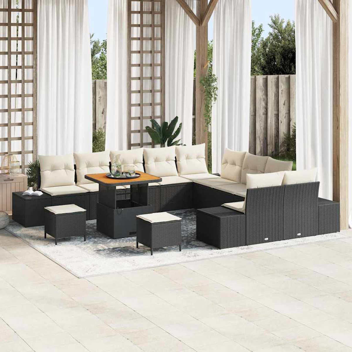 Set patio esterno con mobili in vimini neri, cuscini beige, tavolo in legno e tende bianche sullo sfondo. La scena è luminosa.