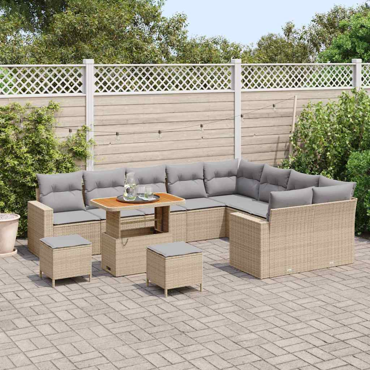 Outdoor-Ecksofa mit grauen Kissen, einem Holztisch und zwei Ottomanen auf einer Steinterrasse, vor einem Zaun und Grün.