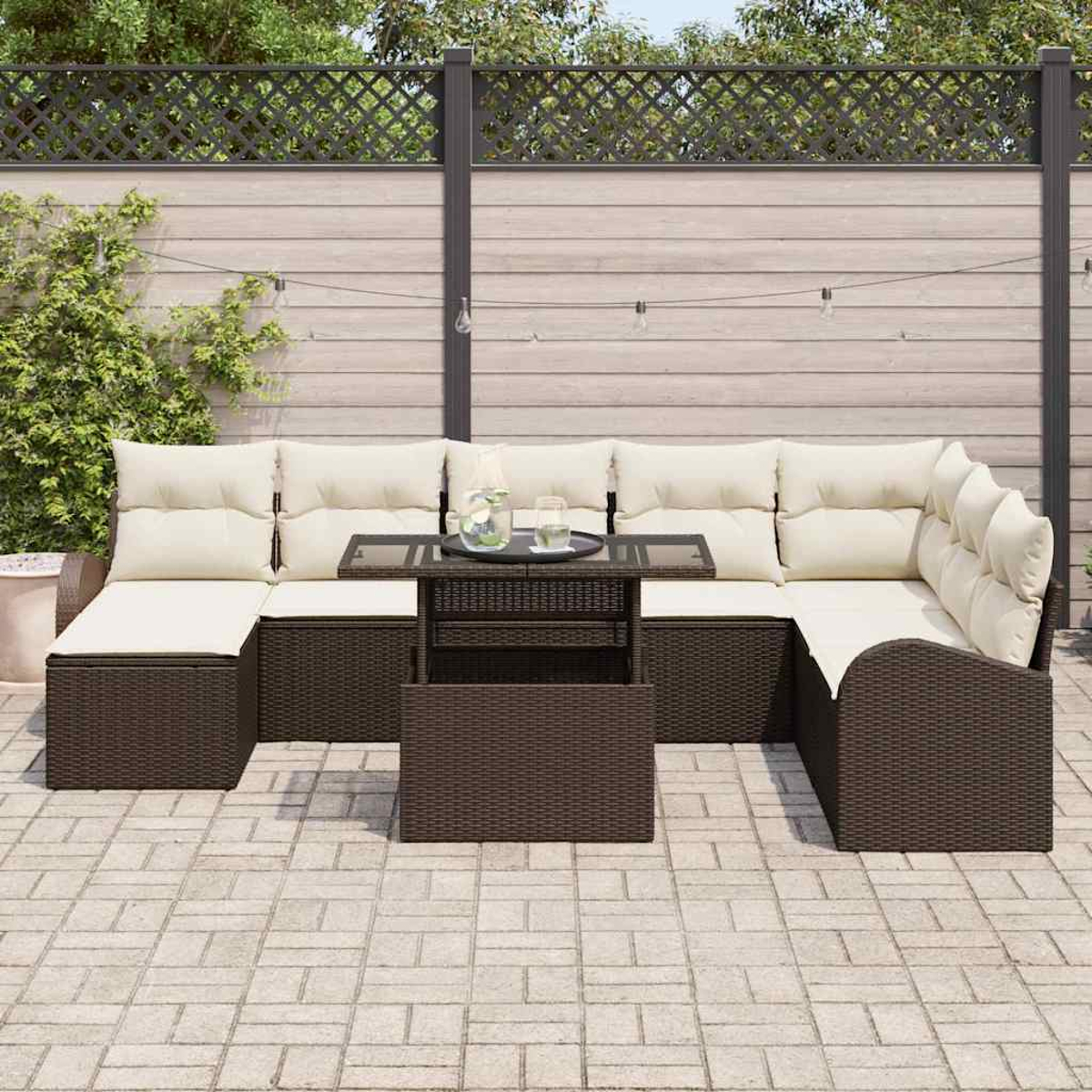 Garten-Terrassenset mit braunen Korbmöbeln und beigefarbenen Kissen. Ein kleiner Tisch mit Getränken steht vor dem Set. Hintergrund: Zaun.