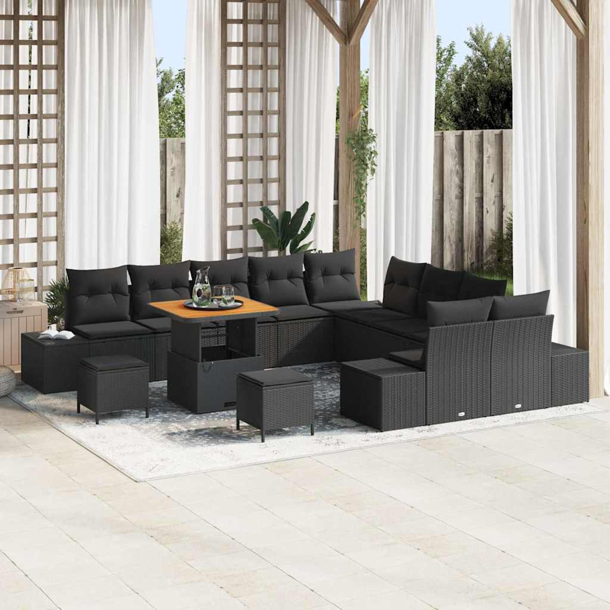 Outdoor-Sitzgruppe mit schwarzen Kissen und einem Holztisch. Weiße Vorhänge und eine Pergola rahmen die Szene mit Gartenblick ein.