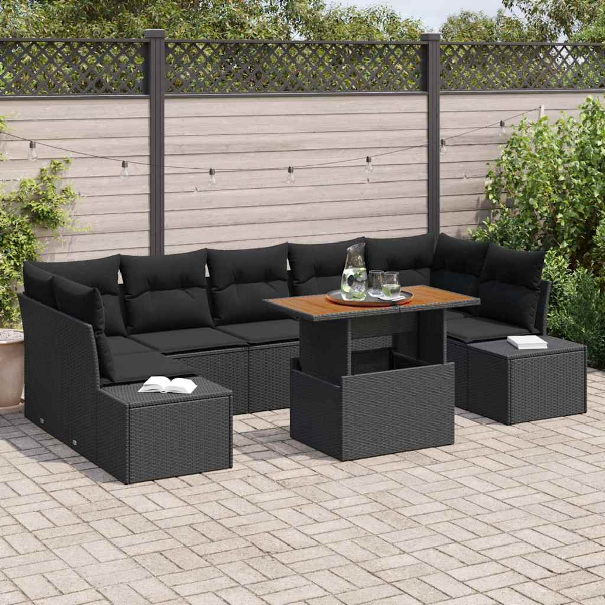 Schwarzes Ecksofa mit Kissen, Tisch und Krug mit Gläsern im Freien. Auf einer Terrasse mit Zaun und Pflanzen im Hintergrund.