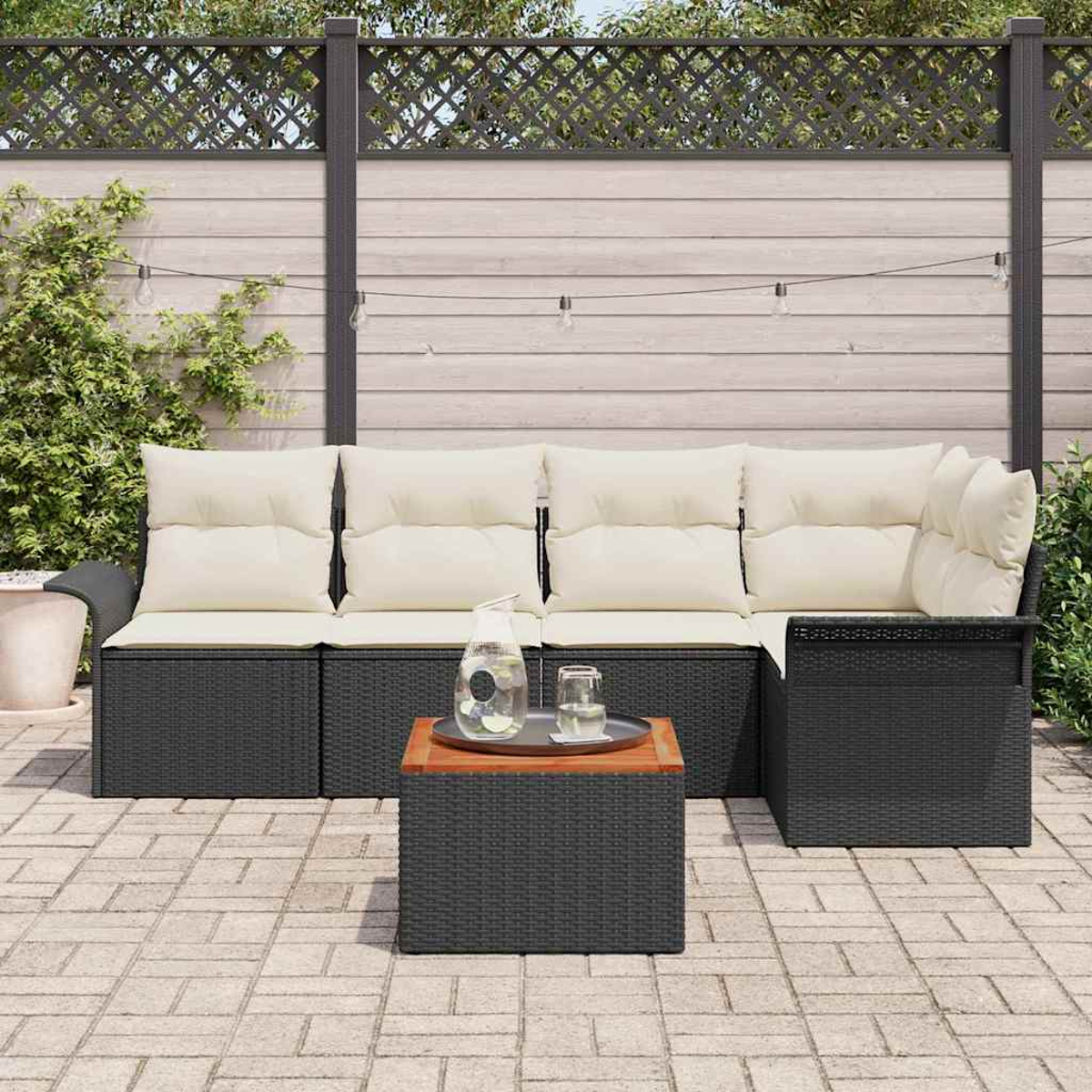 Garten-Sitzgruppe mit schwarzem Korbgeflecht und cremefarbenen Kissen. Inklusive Tisch mit Wasserglas und Krug. Auf einer Terrasse.