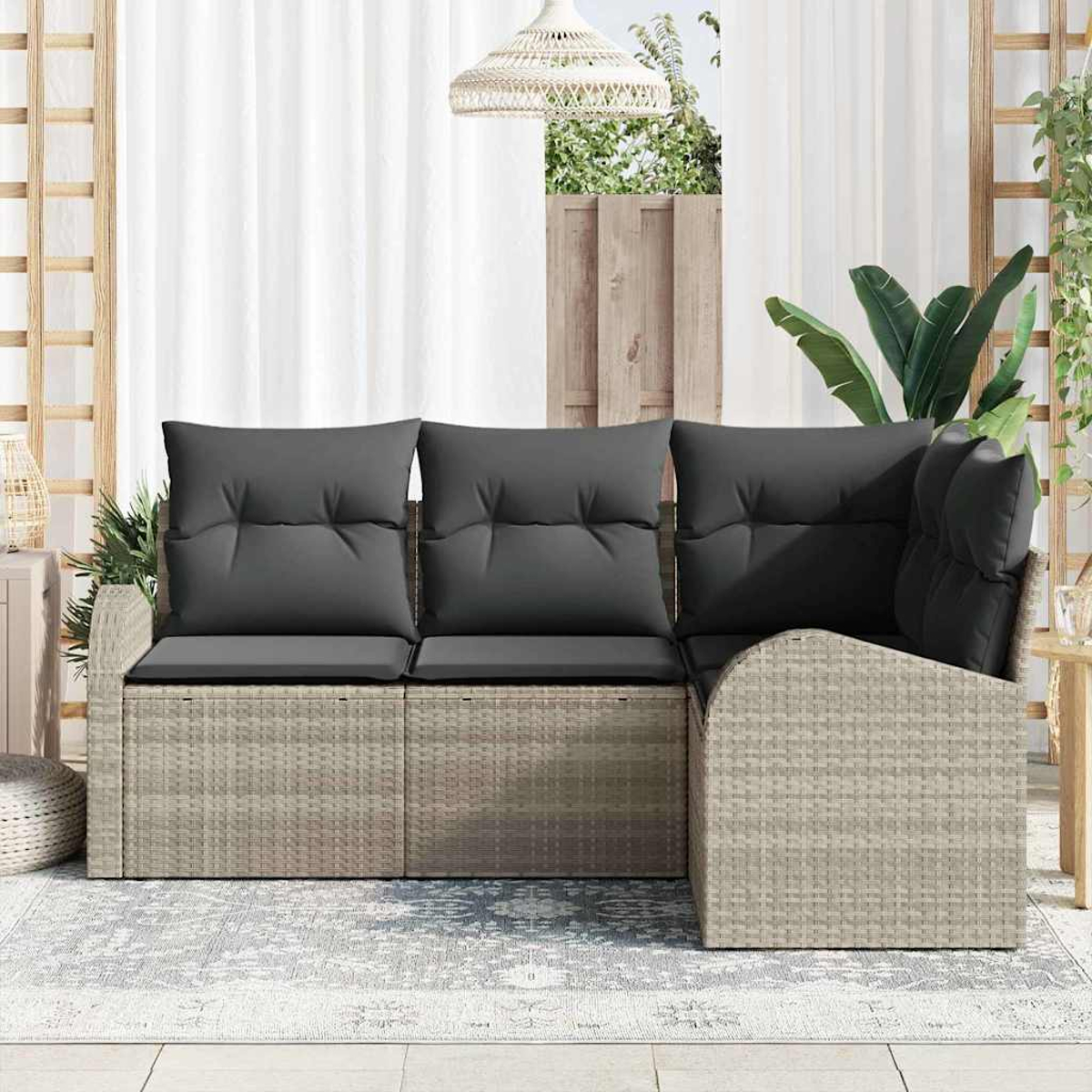 Ein Outdoor-Sofa aus Korbgeflecht mit dunkelgrauen Kissen steht auf einem Teppich. Ein weißer Vorhang und eine Holzkonstruktion sind im Hintergrund.