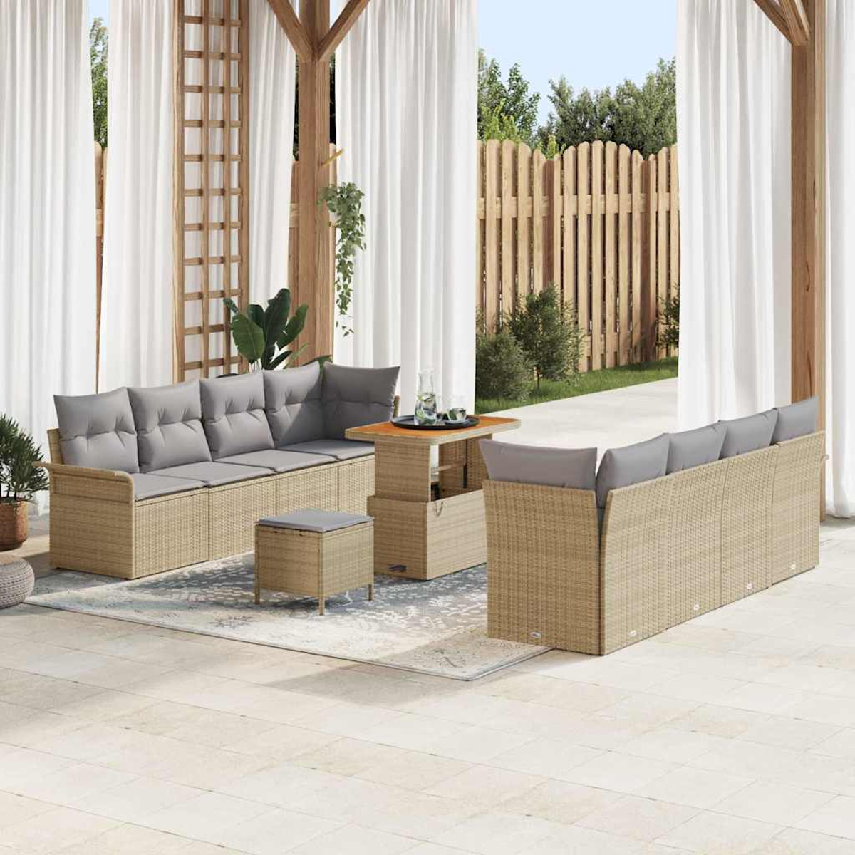 Terrassenmöbel-Set mit Rattan-Sofas, grauen Kissen, einem Tisch und einem Hocker. Weiße Vorhänge und ein Holzzaun sind im Hintergrund.