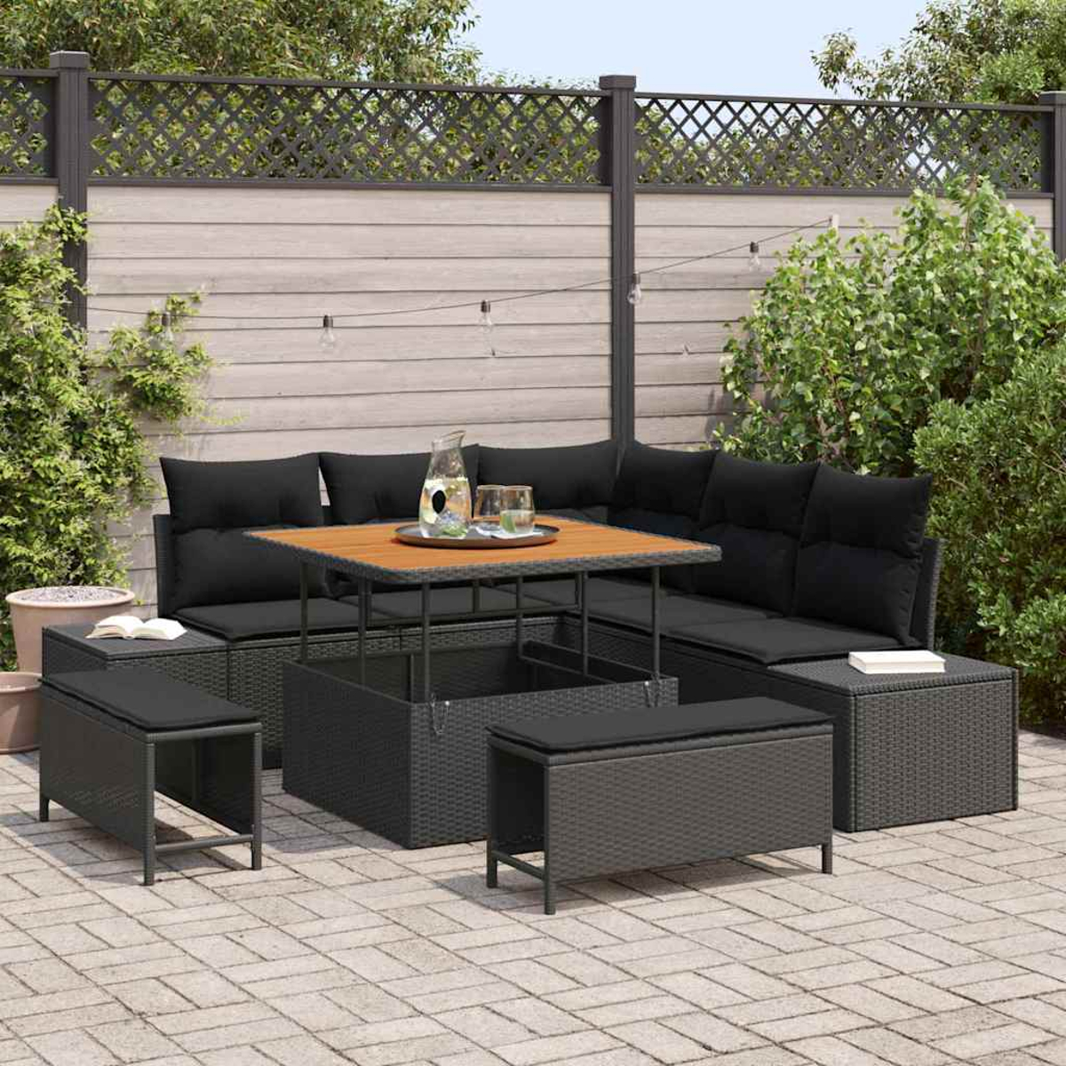 Garten-Terrassenset mit schwarzen Kissen, einem Holztisch und mehreren Bänken. Das Set steht auf einer Ziegelterrasse, im Hintergrund ein Holzzaun.