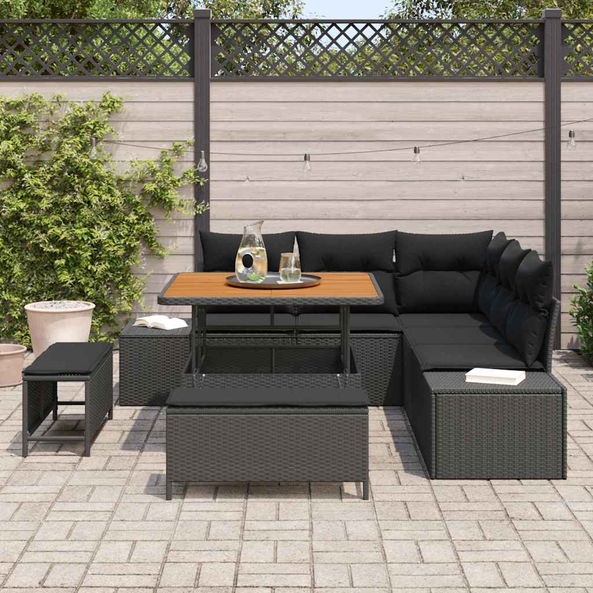 Outdoor-Terrassenset mit schwarzen Kissen, Holztisch und grauen Korbmöbeln auf einer Ziegelterrasse. Hintergrund hat einen Holzzaun.