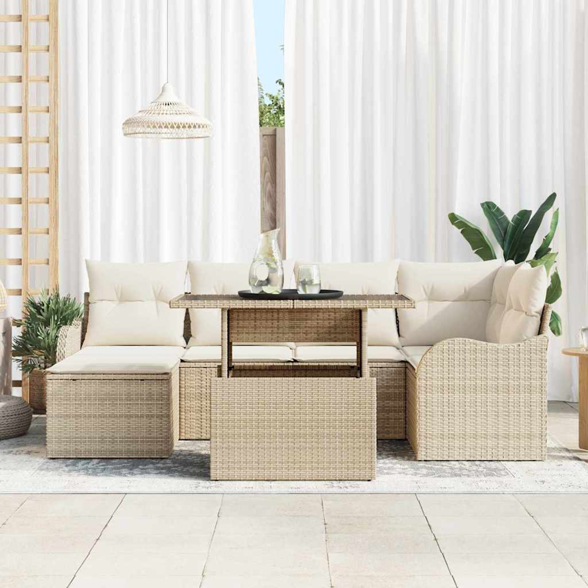 Gartenmöbel-Set aus Korbgeflecht mit cremefarbenen Kissen, Tisch mit Gläsern und Hängelampe vor weißen Vorhängen.